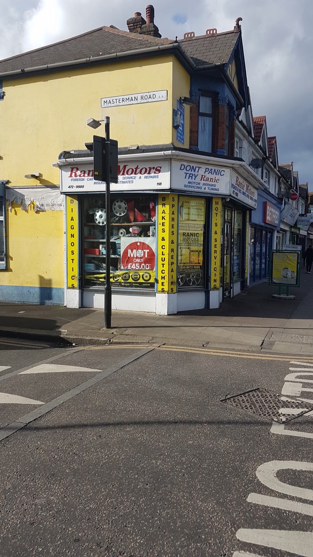 The Ranic Motors corner unit on the High Street South parade in East Ham, next to Betfred, with an MOT price sign in the window.